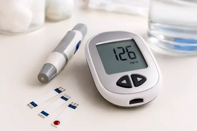 qué es un Glucómetro portátil con pantalla de resultado de glucosa, tiras reactivas y lanceta sobre superficie blanca, herramientas de automonitoreo de glucemia para personas con diabetes.